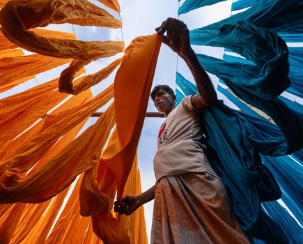a textile worker in Narayanganj, Bangladesh, carefully arranging freshly dyed fabrics on wooden frames