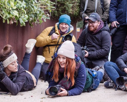 A group of people with cameras in hand, some laying on the floor, some crouching or standing