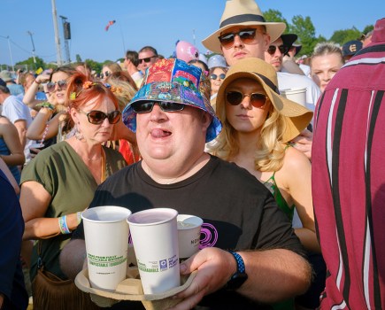 man at a festival wearing a bucket hat carrying container of paper cups